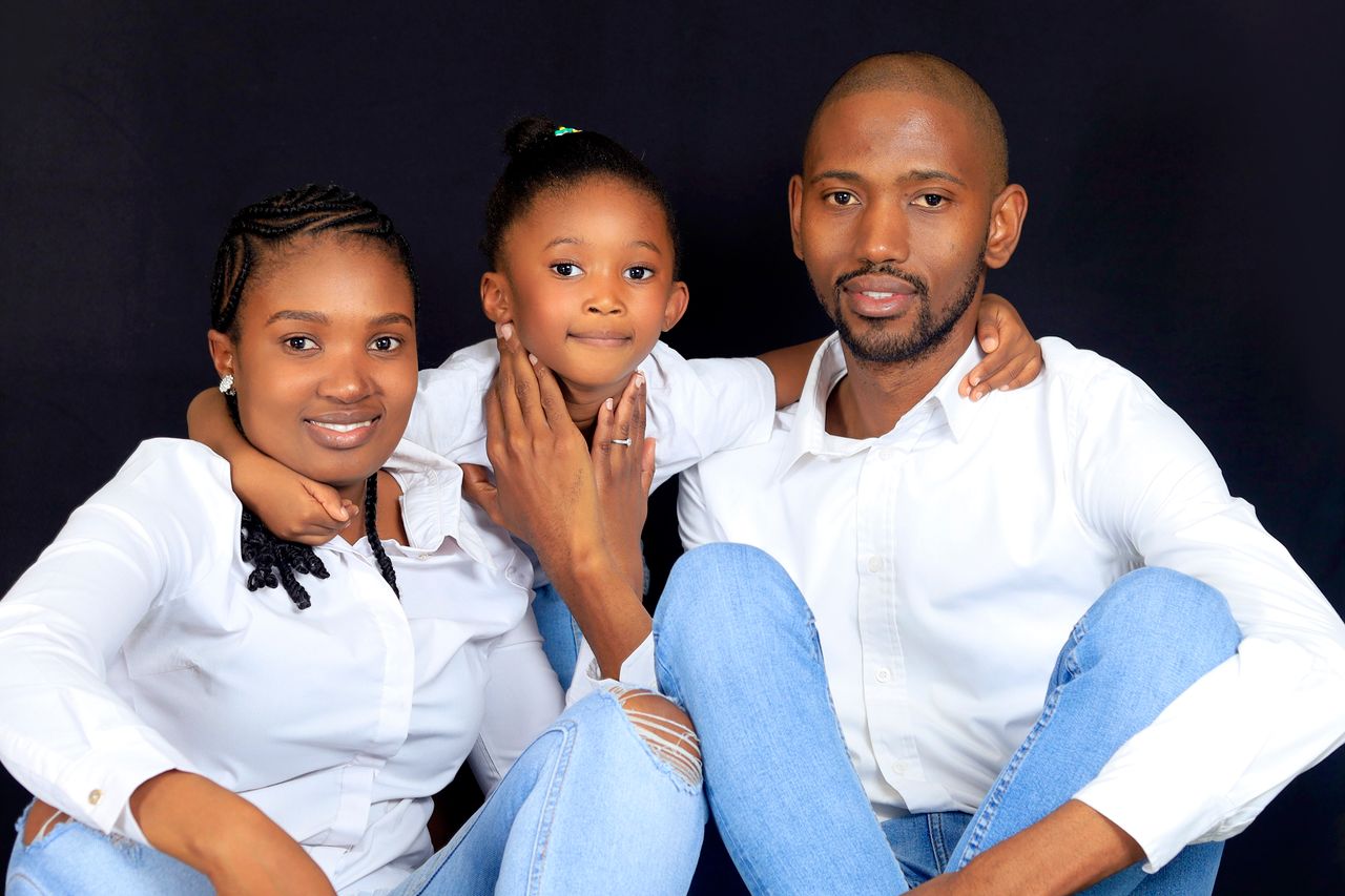 A joyful family of three posing together in studio with smiles.