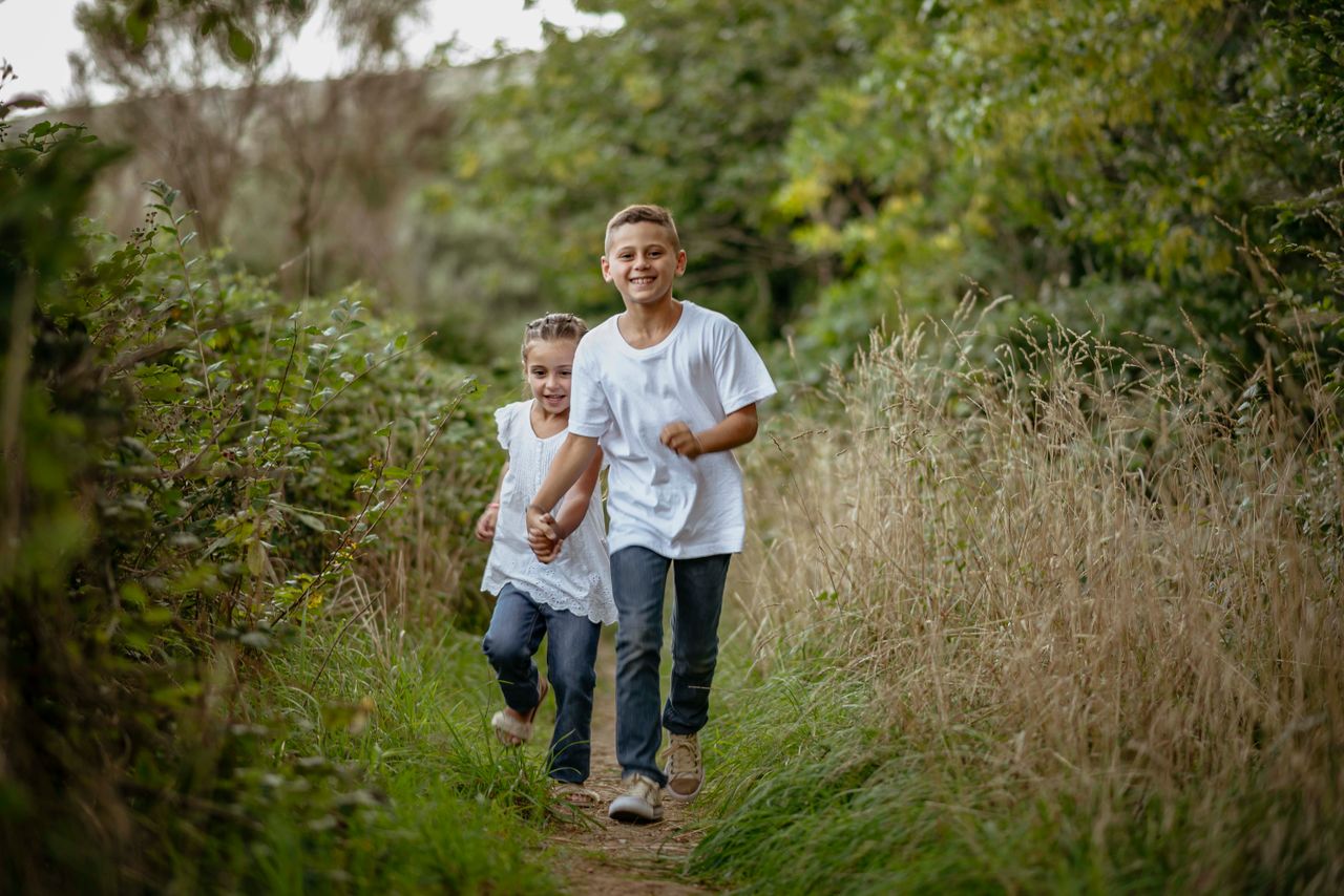 Two happy children running down a nature trail surrounded by lush greenery in summer.