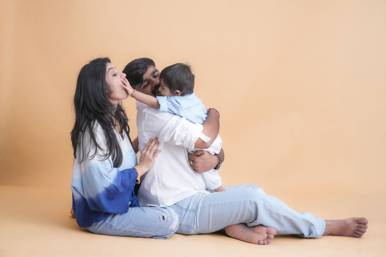 A family of three sharing a joyful moment in a cozy indoor environment with a warm backdrop.
