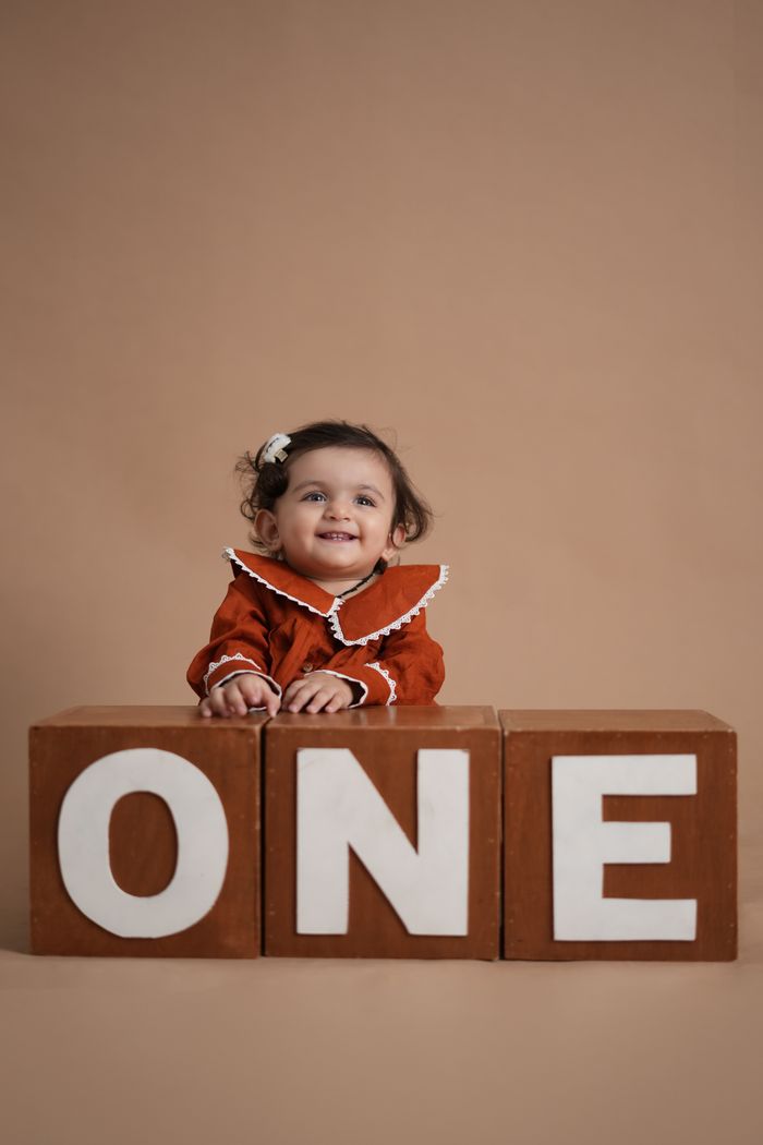 A smiling baby celebrates first birthday with 'ONE' spelled out in wooden blocks. Perfect for birthday themes.