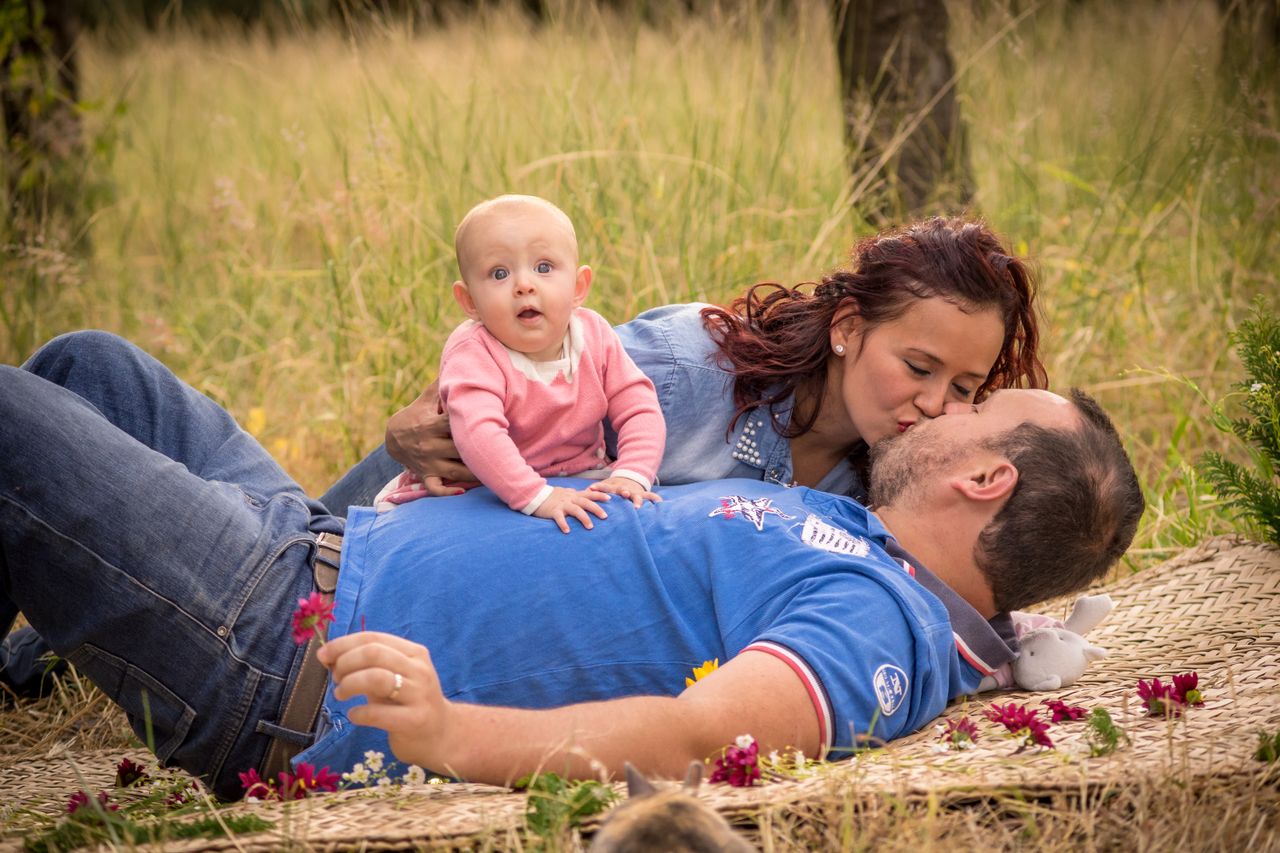 A tender family scene outdoors with parents kissing while their baby lies on the father.